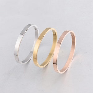 Peut inclure: Trois bracelets simples en argent, or et or rose. Les bracelets sont tous de la même taille et du même style, avec une finition lisse et polie.