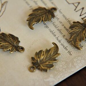 Peut inclure: Quatre breloques en forme de feuille de couleur or antique avec un trou en haut pour la suspension. Les feuilles ont un design d&eacute;taill&eacute; et textur&eacute;.