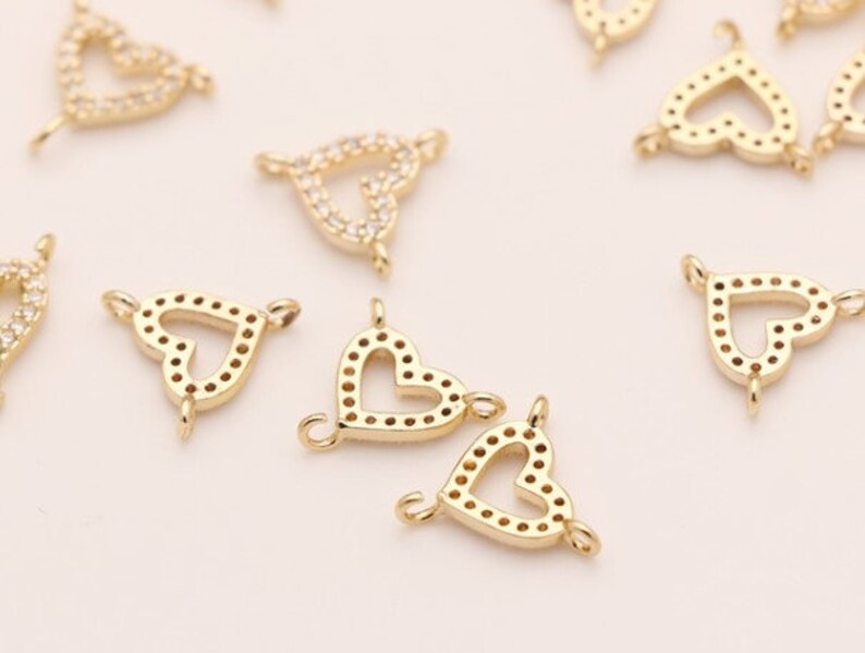 May include: Gold-tone heart-shaped charms with clear crystal accents. The charms have a loop on each side for attaching to jewelry.