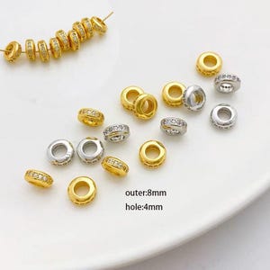 Op de afbeelding: Een verzameling gouden en zilveren ringvormige kralen met heldere strass steentjes. De kralen zijn 8 mm in diameter met een gat van 4 mm. outer:8mm hole:4mm