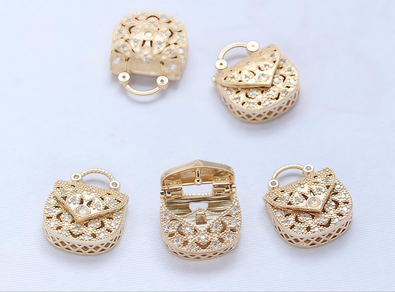 以下が含まれることがあります： 金色のハンドバッグ型のジュエリーパーツ。繊細な透かし彫りとキラキラ光るクリスタルのアクセントが特徴です。留め金や開いたバッグなど、さまざまなデザインがあります。ジュエリー作りやハンドメイドに最適です。