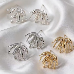 Può includere: Sei orecchini a lobo in tonalità argento e oro, disposti su raso bianco. Gli orecchini presentano un design stilizzato e aperto con più bracci curvi, alcuni adornati con piccole pietre trasparenti. Gli orecchini sono progettati per assomigliare a un fiore.
