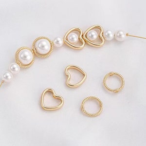 May include: A set of gold-toned jewelry charms featuring a variety of shapes, including hearts and circles. The charms are strung on a chain with white pearls.