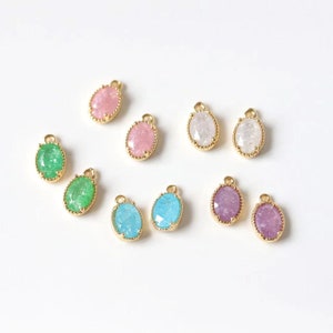 May include: Assortment of oval-shaped, gold-rimmed charms with various colored, glittery glass inserts. The colors include pink, white, green, blue, and purple.