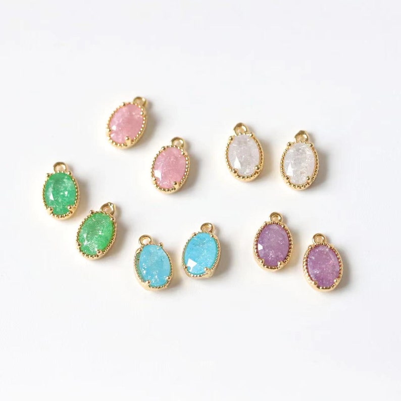 May include: Assortment of oval-shaped, gold-rimmed charms with various colored, glittery glass inserts. The colors include pink, white, green, blue, and purple.