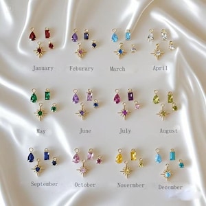 May include: Twelve gold charms with different colored gemstones and starburst designs. Each charm is labeled with a month of the year, from January to December.