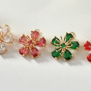 May include: Four gold flower charms with different colored gemstones. The charms are white, red, green, and clear.