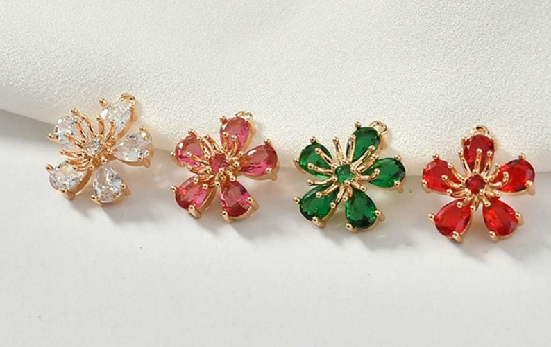 May include: Four gold flower charms with different colored gemstones. The charms are white, red, green, and clear.