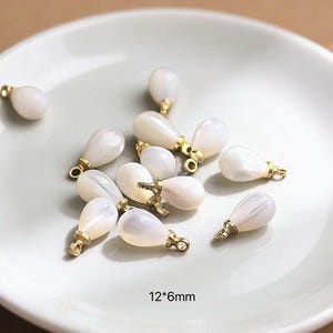 May include: A collection of teardrop-shaped, off-white beads with gold-colored metal accents. The beads are arranged on a white plate. The text "12*6mm" is visible at the bottom of the image, indicating the size of the beads.