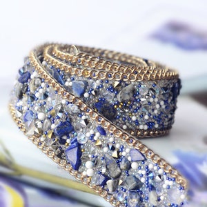 Könnte beinhalten: Nahaufnahme einer blauen und goldenen Perlenborte mit kettenartigem Design. Die Borte ist aus kleinen blauen und weißen Perlen, goldenen Perlen und kleinen blauen Steinen gefertigt.