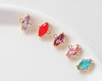Puede incluir: Cinco colgantes de gemas en forma de marquesa de colores en fila. Cada colgante tiene un engaste dorado con un pequeño lazo en la parte superior para sujetarlo a la joyería. Las gemas son moradas, rojas, rosas y turquesas.
