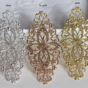 Könnte beinhalten: Drei verzierte filigranartige Metallverzierungen in Silber, Gold und Messing. Jedes Stück zeigt ein zartes Blumenmuster mit einer zentralen Blume und filigranen Details.