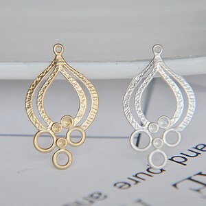 May include: Two ornate teardrop-shaped pendants, one gold-toned and one silver-toned, with a textured design. Each pendant features a loop at the top and a cluster of small circles at the bottom. These are likely jewelry components.