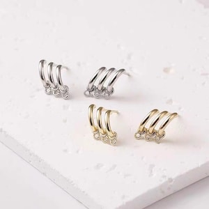 Pode incluir: Três pares de brincos com um design curvo. Os brincos são feitos de metal prateado e dourado. Cada brinco tem três argolas curvas com um pequeno laço na parte inferior.