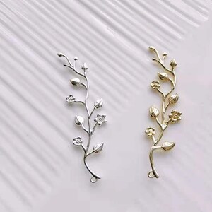 May include: Two silver and gold floral branch charms with delicate leaves and flowers. These charms are perfect for adding a touch of elegance to jewellery projects.