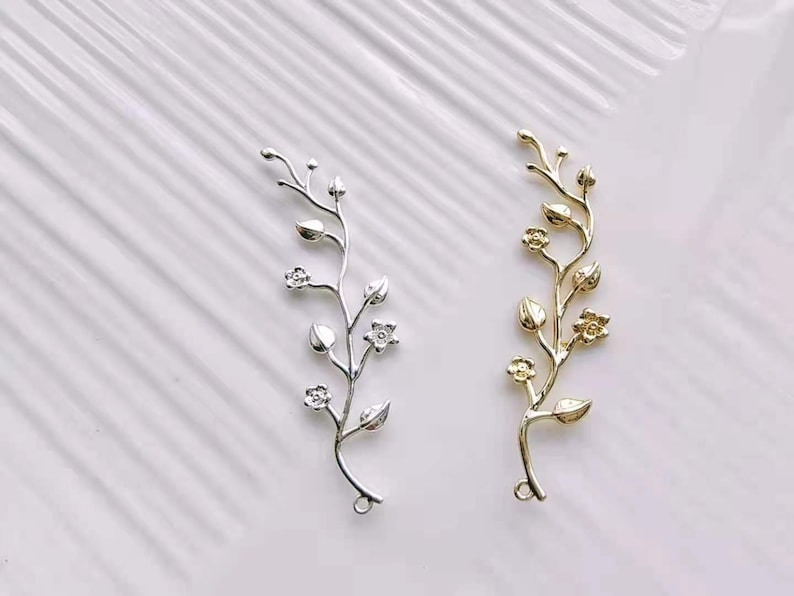 May include: Two silver and gold floral branch charms with delicate leaves and flowers. These charms are perfect for adding a touch of elegance to jewellery projects.