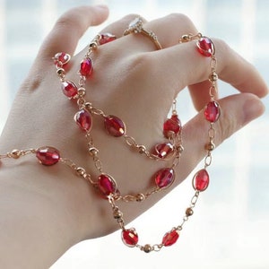 May include: A gold chain necklace with red oval-shaped beads. The necklace is layered and has a delicate design.