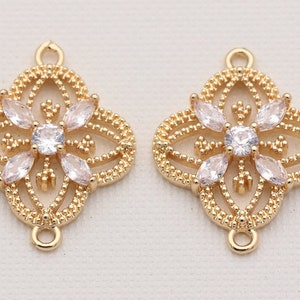 May include: Two gold-tone metal charms with a decorative, openwork design featuring a central clear rhinestone and smaller rhinestones around the edges. Each charm has two loops for attaching to jewelry.