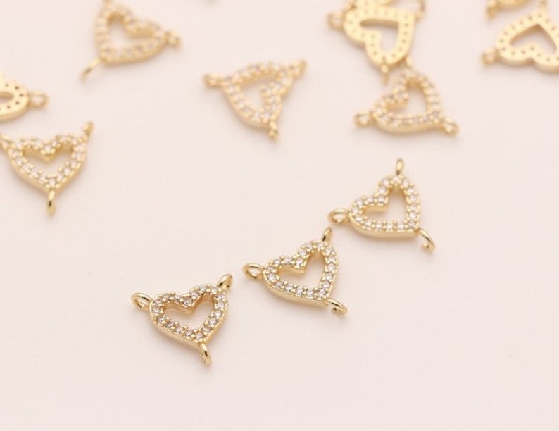 May include: A group of gold-tone heart-shaped charms with clear crystal accents. Each charm has a loop at the top for attaching to jewelry.