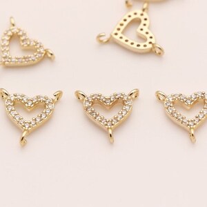 May include: Five gold-tone heart-shaped charms with clear crystal accents. Each charm has a loop on the top and bottom for attaching to jewelry.