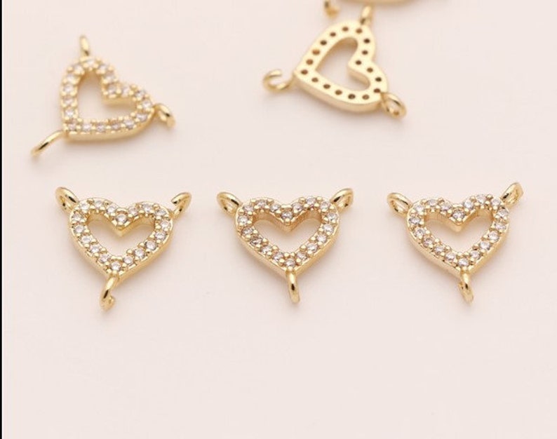 May include: Five gold-tone heart-shaped charms with clear crystal accents. Each charm has a loop on the top and bottom for attaching to jewelry.