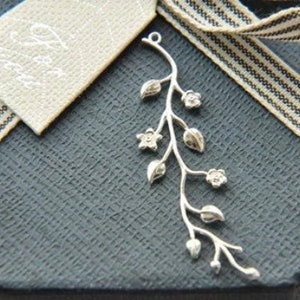 May include: Silver pendant featuring a delicate branch with leaves and flowers. The pendant is on a dark grey background with a white and black striped ribbon.