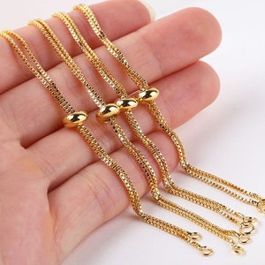 May include: Four gold chain bracelets with adjustable sliding beads. The chains are delicate and have a box chain design.