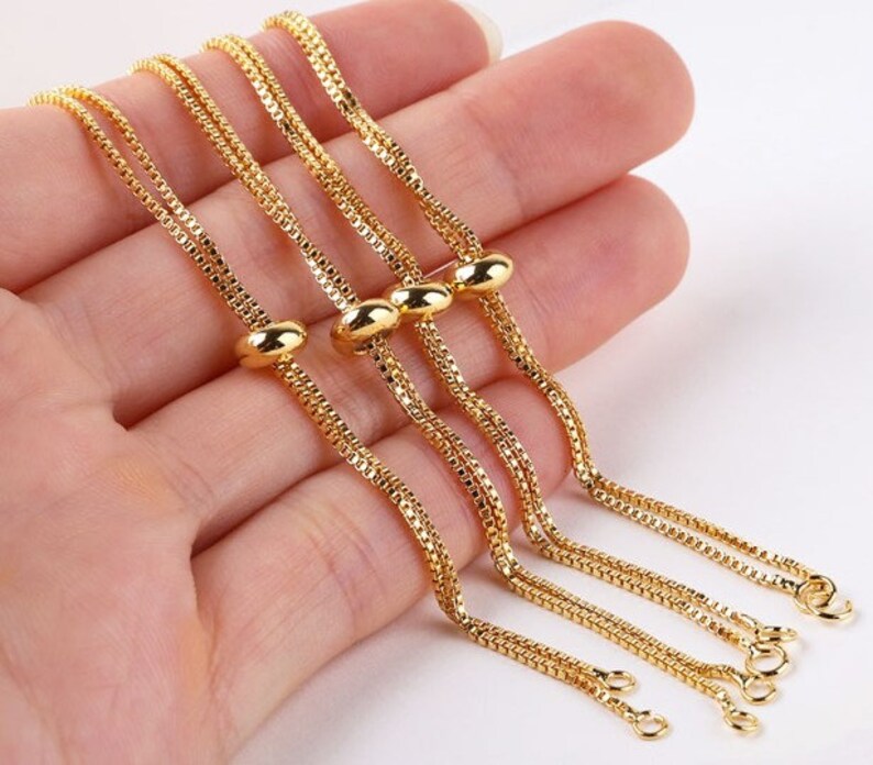 May include: Four gold chain bracelets with adjustable sliding beads. The chains are delicate and have a box chain design.