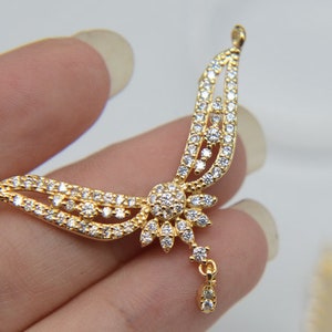 May include: Gold pendant with a delicate, intricate design featuring a flower with a dangling drop. The pendant is adorned with clear cubic zirconia stones.