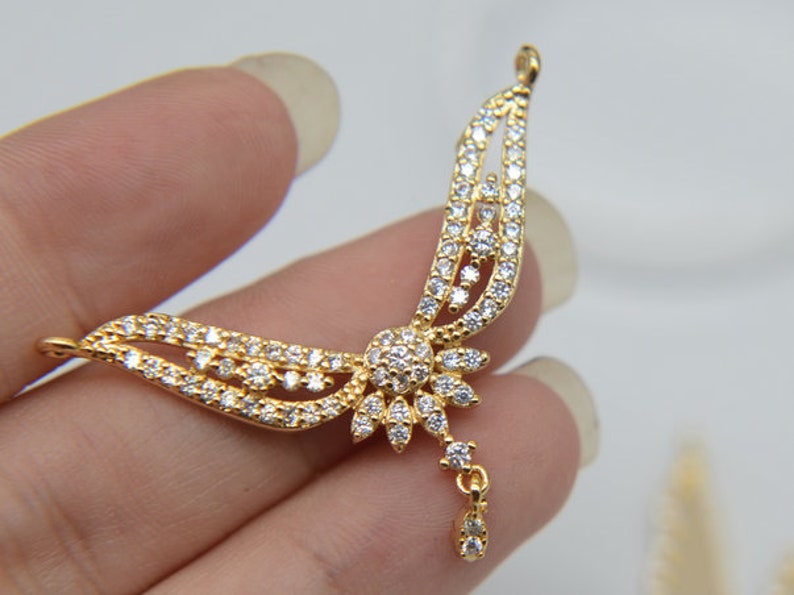 May include: Gold pendant with a delicate, intricate design featuring a flower with a dangling drop. The pendant is adorned with clear cubic zirconia stones.