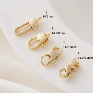 Könnte beinhalten: Vier goldfarbene Metallverschlüsse zum Schmuckbasteln. Die Verschlüsse sind in verschiedenen Größen und Formen, darunter ein einfaches Oval, eine Kleeblattform, eine rechteckige Form und eine Elefantenform. Die Verschlüsse sind auf weißem Hintergrund abgebildet.