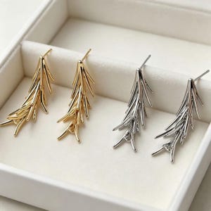 Peut inclure: Deux paires de boucles d'oreilles à tige en forme de branches de pin. Une paire est finie dans un ton doré poli et l'autre paire est finie dans un ton argenté poli. Chaque boucle d'oreille présente plusieurs segments fins et pointus.