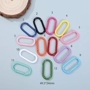 May include: Twelve colourful metal key rings in various colours, including blue, black, pink, red, orange, yellow, white, green, and light blue. The key rings are arranged in a circle on a light grey surface. The key rings are 49.5 mm by 24 mm.