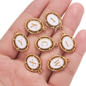 Puede incluir: Ocho abalorios ovalados de color dorado con esmalte blanco y letras doradas. Las letras son I, K, Y, C, L, X, W.