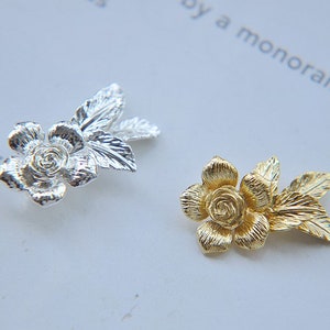 May include: Two metal rose flower embellishments with leaves. One is silver and the other is gold.