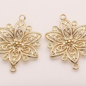 May include: Two gold-tone metal flower-shaped pendant charms with three loops for attaching to jewelry. The charms have a delicate filigree design.