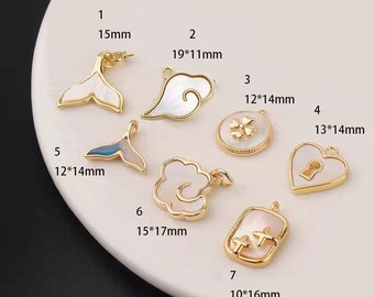 May include: Seven gold-tone pendants with white shell inlays. The pendants feature various shapes, including a mermaid tail, a cloud, a flower, a heart with a keyhole, a circle with a four-leaf clover, and a rectangle with a cross. The pendants are labeled with numbers 1 through 7 and their dimensions in inches.