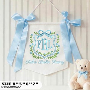 May include: A white fabric wall banner featuring an embroidered light blue monogram FRL inside a shield, surrounded by a green leaf and blue flower wreath. The text Fisher Larkin Rainey is embroidered below. It has light blue satin ribbon bows.