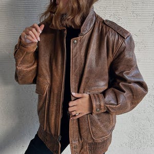 Jaqueta bomber oversized de couro marrom estilo anos 90, casaco aviador com efeito desgastado e bolsos utilitários aplicados.