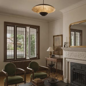 Puede incluir: Una l&aacute;mpara colgante de metal oscuro con una pantalla ancha y poco profunda en forma de platillo con un acabado interior dorado met&aacute;lico, suspendida de una varilla delgada, que ilumina hacia abajo una habitaci&oacute;n con dos sillones de terciopelo verde.