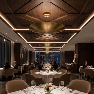 May include: A restaurant interior featuring a series of large, circular, brushed brass pendant lights suspended from a dark wood coffered ceiling with integrated linear lighting. The dining room is furnished with white-clothed tables and chairs.