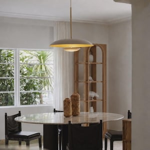 Puede incluir: Una l&aacute;mpara colgante con una pantalla de c&uacute;pula ancha y poco profunda en color beige mate y un interior dorado, suspendida por una varilla delgada desde un dosel de techo a juego. La luz emite un brillo c&aacute;lido hacia abajo.
