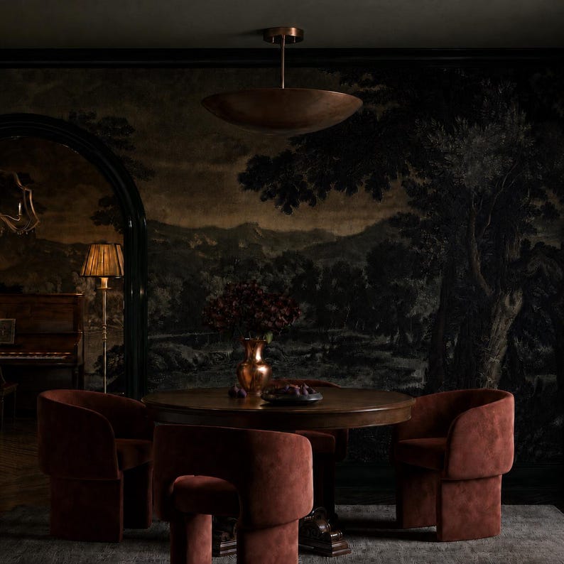 May include: A round wooden dining table surrounded by four rust-colored upholstered chairs with curved backrests. A copper-toned bowl sits on the table next to a vase. A large copper pendant light hangs above, and a floor lamp stands nearby.