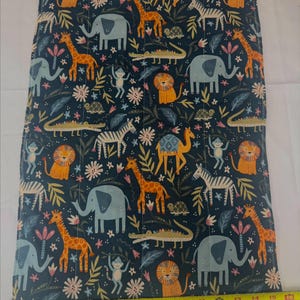 May include: A rectangular fabric piece with a dark blue background featuring a repeating pattern of orange lions, yellow giraffes, light blue elephants, zebras, crocodiles, monkeys, and turtles. A yellow measuring tape shows a width of 16 inches.