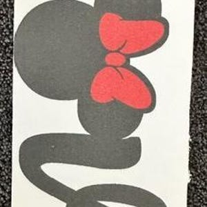 May include: A rectangular white vinyl decal featuring the word Love in a black cursive script font. The letter o is replaced by a black silhouette of a mouse head with a red bow. The decal has a circular cutout at the top for hanging.