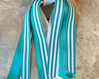 May include: A set of teal and white striped ribbon hair ties. The ribbons are tied together in the centre with a white ribbon.