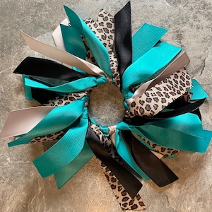 May include: A teal, black, and silver ribbon hair tie with a leopard print pattern.