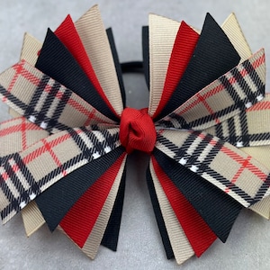 May include: A large plaid bow with black, red, and beige ribbon. The bow is tied with a red ribbon in the center.