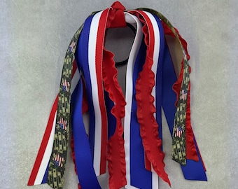 May include: A red, white and blue ribbon hair tie with a camouflage ribbon. The hair tie is made of multiple ribbons tied together.