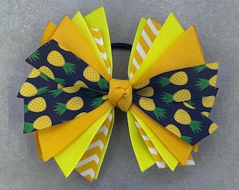 May include: A yellow and green pineapple print hair bow with a yellow and white striped ribbon. The bow is tied with a black elastic band.